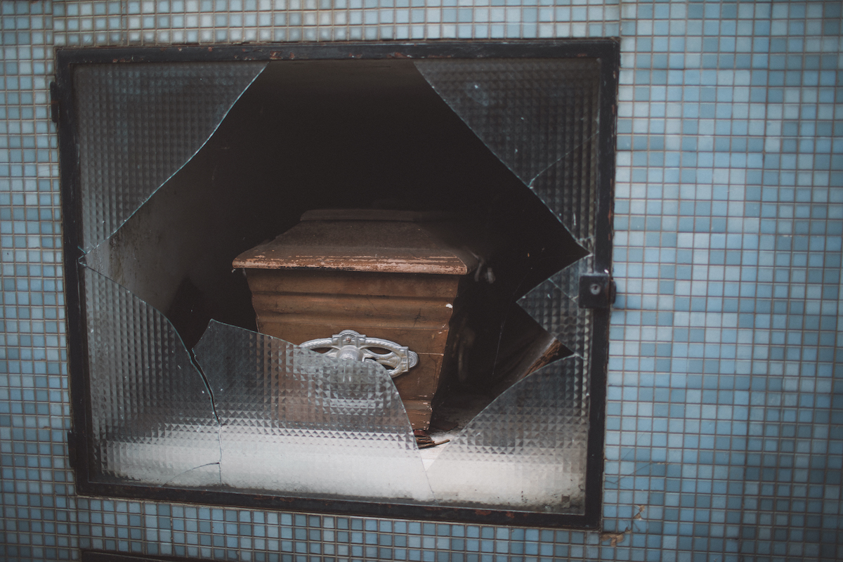 A photo of a casket inside a vertical tomb behind a smashed glass panel.