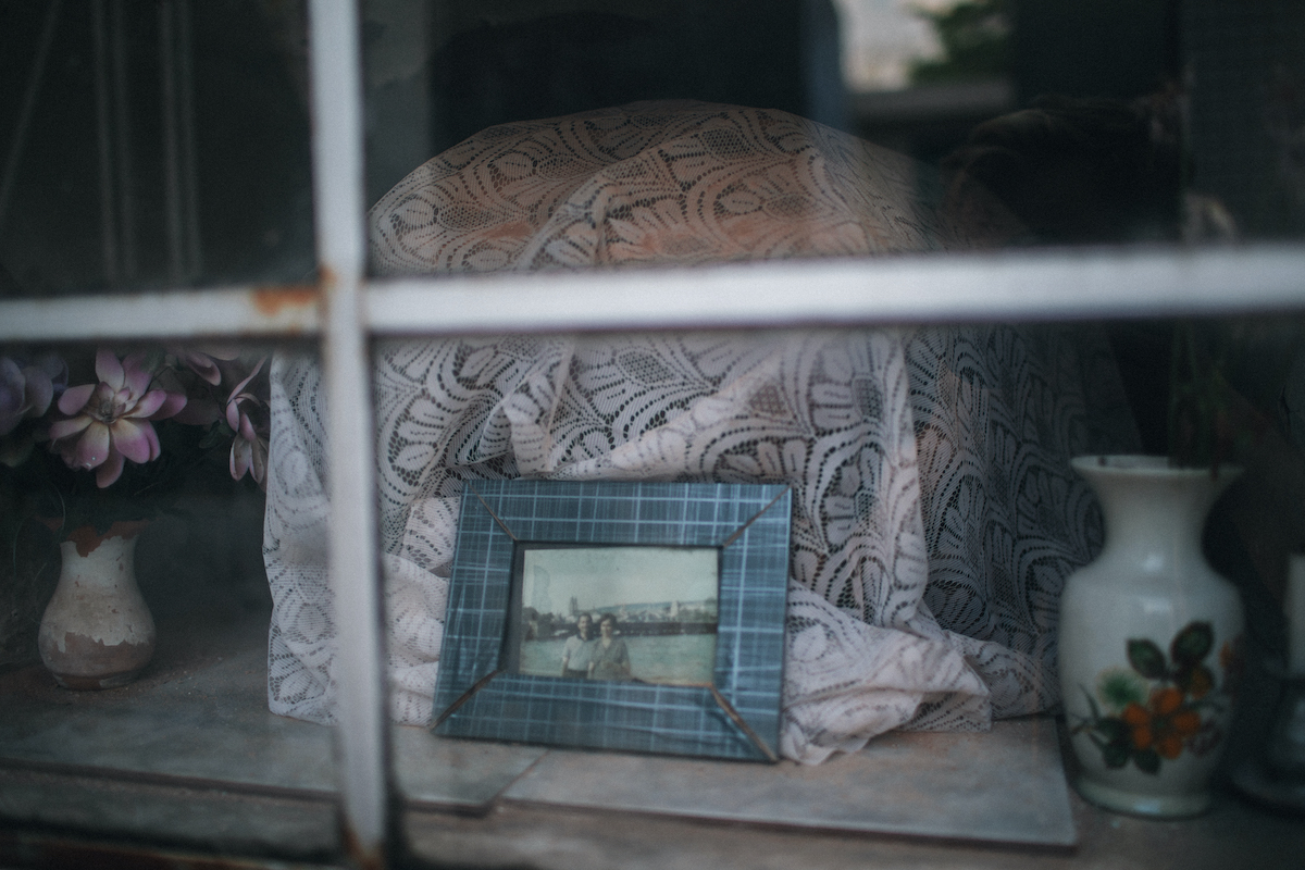 A photo of a casket behind a glass window, covered in a piece of lacy white fabric, with a small framed picture depicting two people.