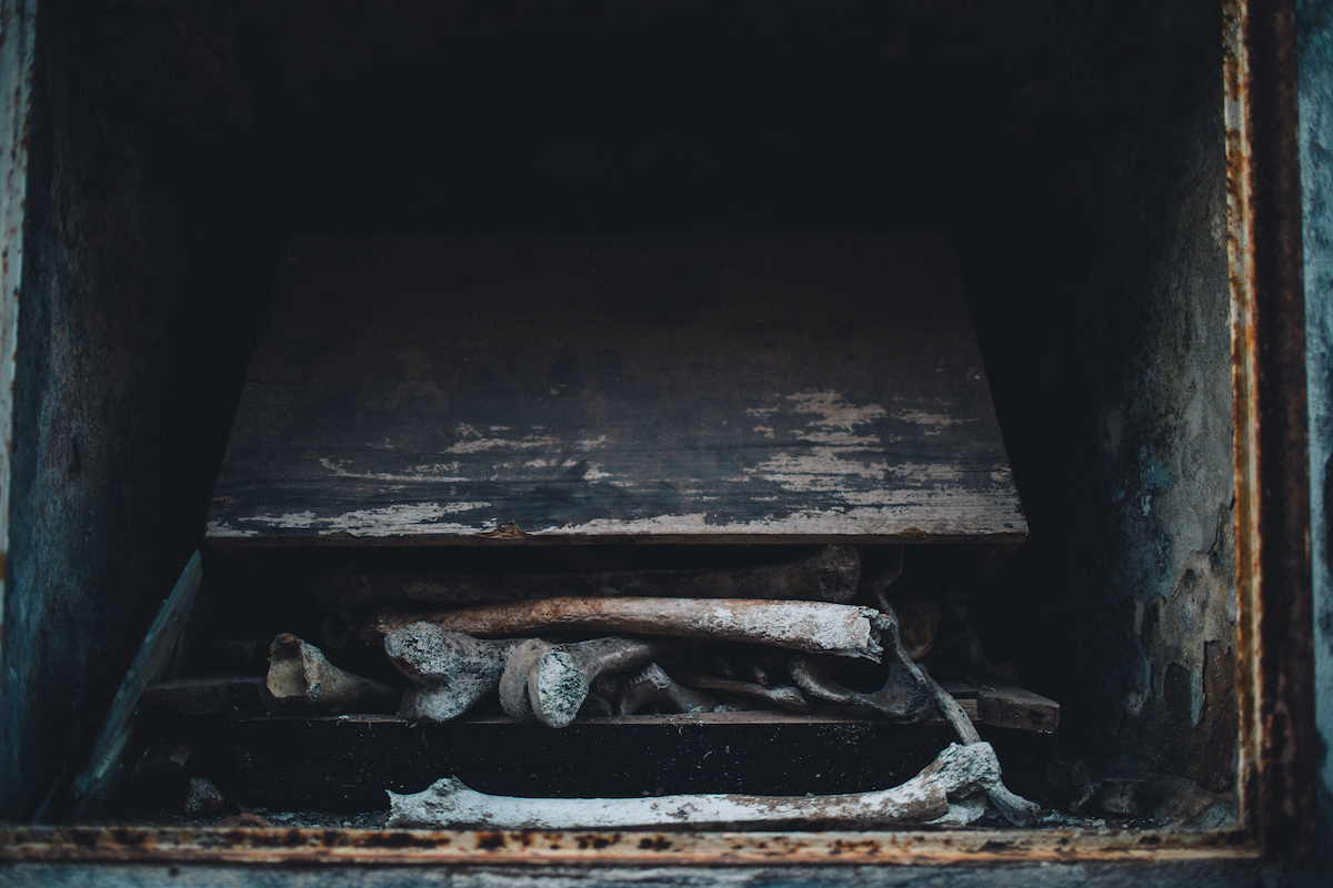 A photo of a wooden casket opened up with bones spilling out of it.