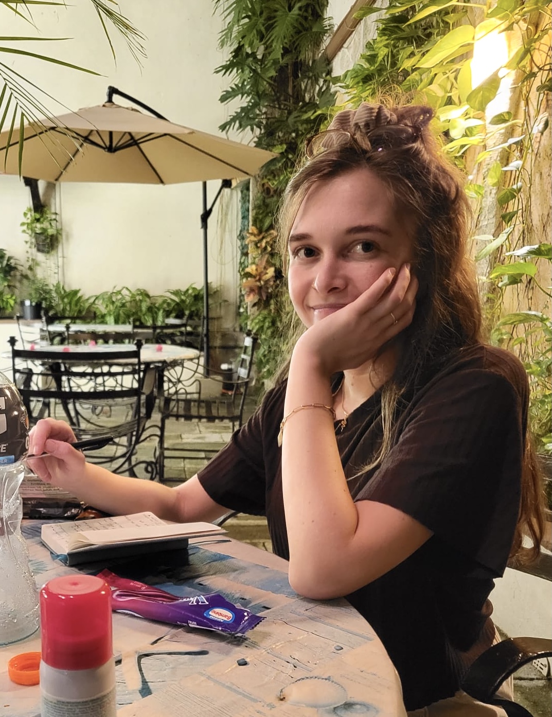 Photo of a young woman with light long hair, sitting at a table and writing something in a journal.