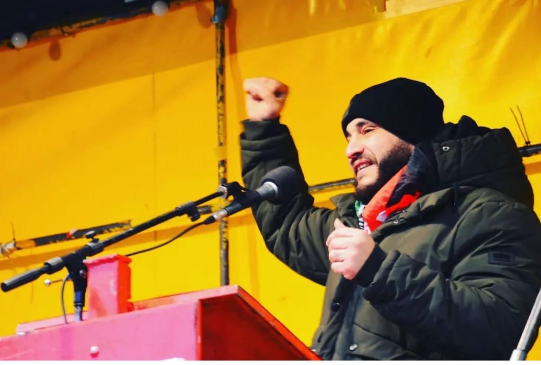 Photo of a bearded man speaking on a stage with a microphone.