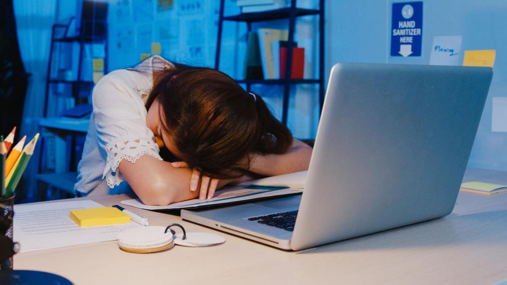 Een foto van een vrouw aan een bureau voor haar laptop, met haar hoofd op haar armen