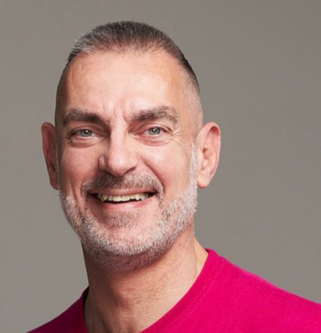 Testosterone gel, masculinity, Netherlands - Man with grey hair and beard smiles at the camera, wearing a pink t-shirt.