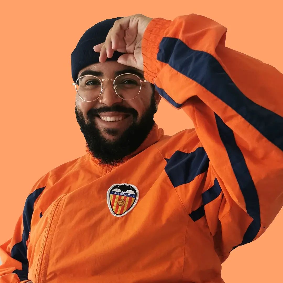 Testosterone gel, masculinity, Netherlands - Bearded man wearing round glasses, a beanie hat, and a bright orange jacket smiles at the camera.