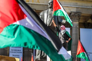 ​A protestor at a pro-Palestinian march in Melbourne wears a keffiyeh and waves a palestinian flag.