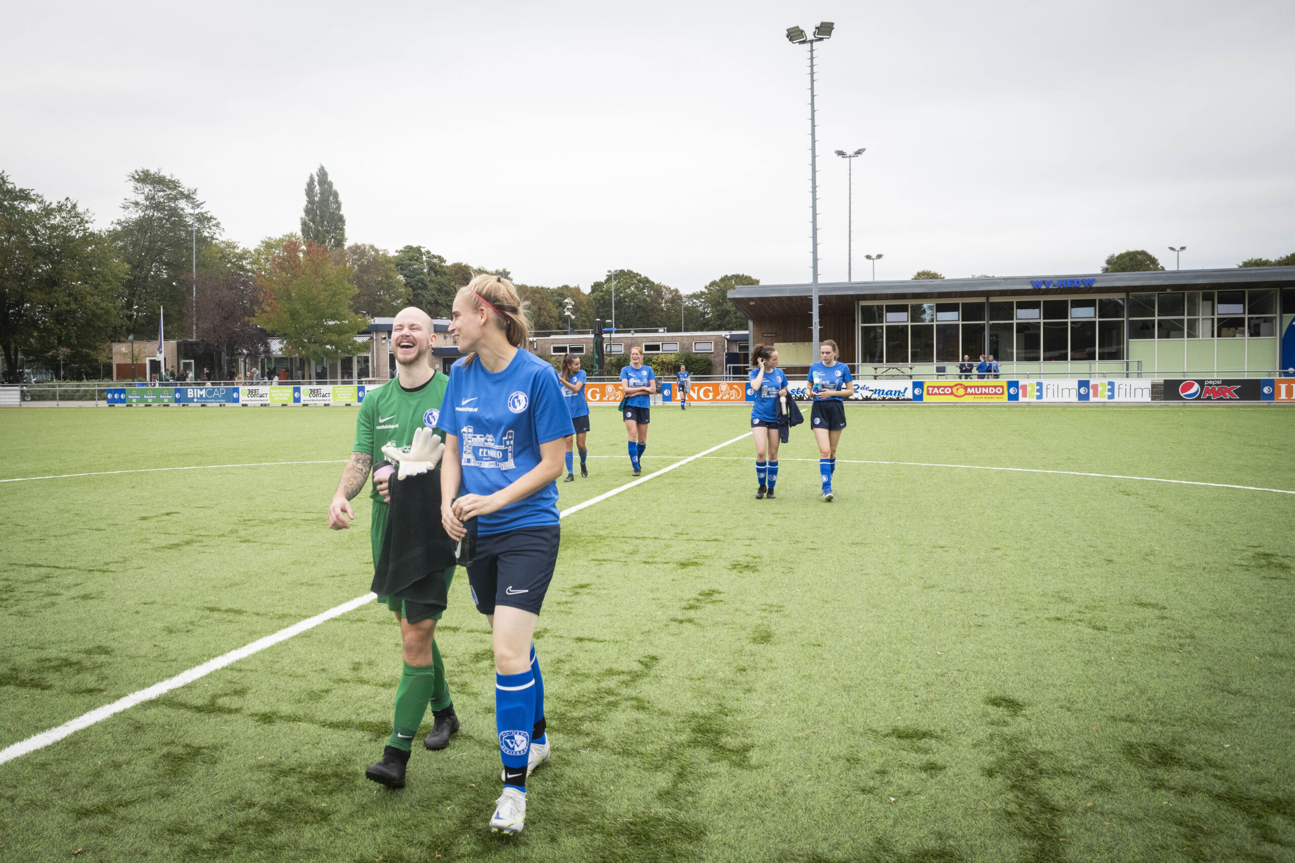 players walking across a football pitch, the team wears a bue jersey and the goal keeper's jersey is green