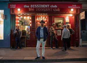 Taha Siddiqui, Dissident Club Paris – man wearing a fedora standing in front of a cafe front painted red.