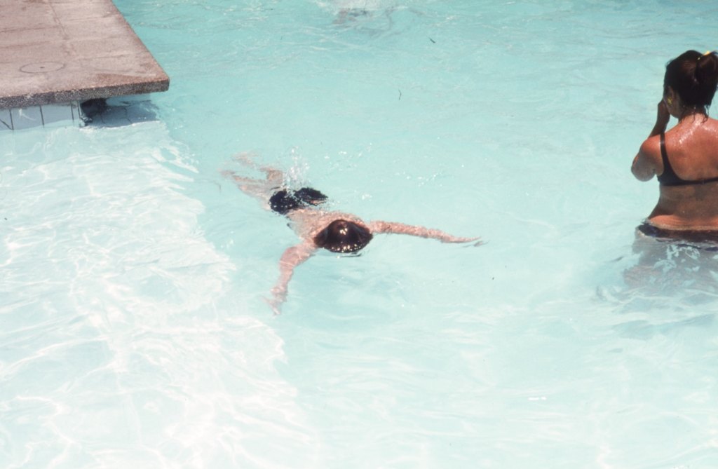 an adult woman in a black bikini and a kid swimming in a blue outdoor swimming pool