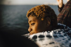 Young Black non-binary person looking away at pier, they ha