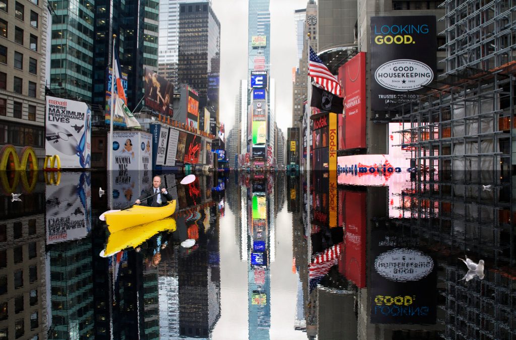 A businessman in a kayak travelling down flooded Times Square.