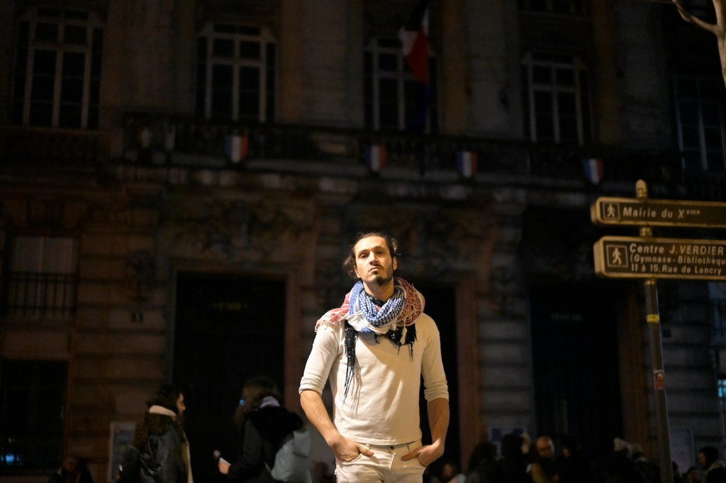 A photo of a young Palestinian man standing in the street, wi