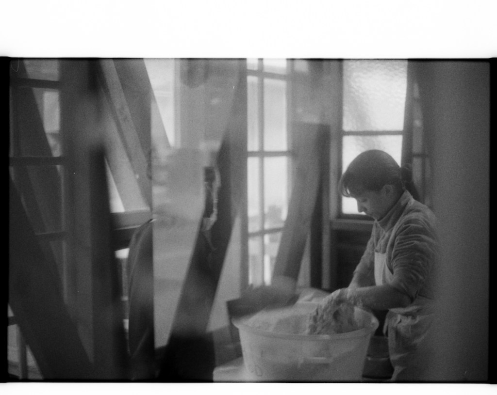 militant bakers - black and white blurry picture of a young woman making bread dough in a room with big windows