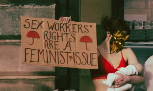 stripper in a red bra and mask holding a protest sign and a baby in Edinburgh