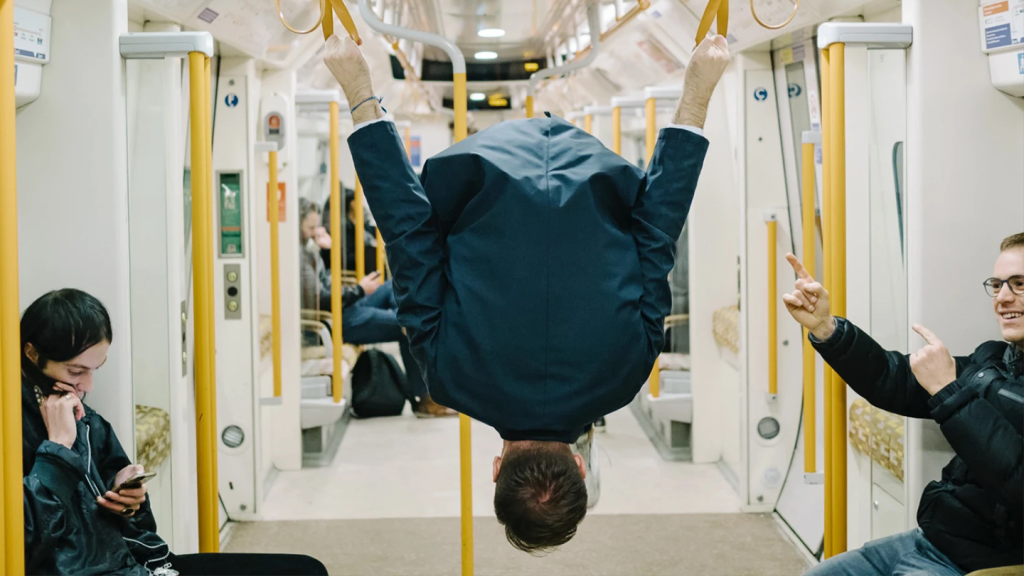 A photo of a man doing a twizzle on the roof handles of the london overground