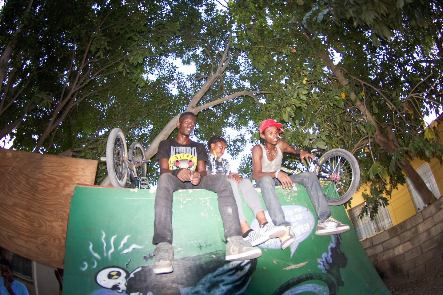 Three people sat on a graffitied ramp with their BMX bikes next to them.