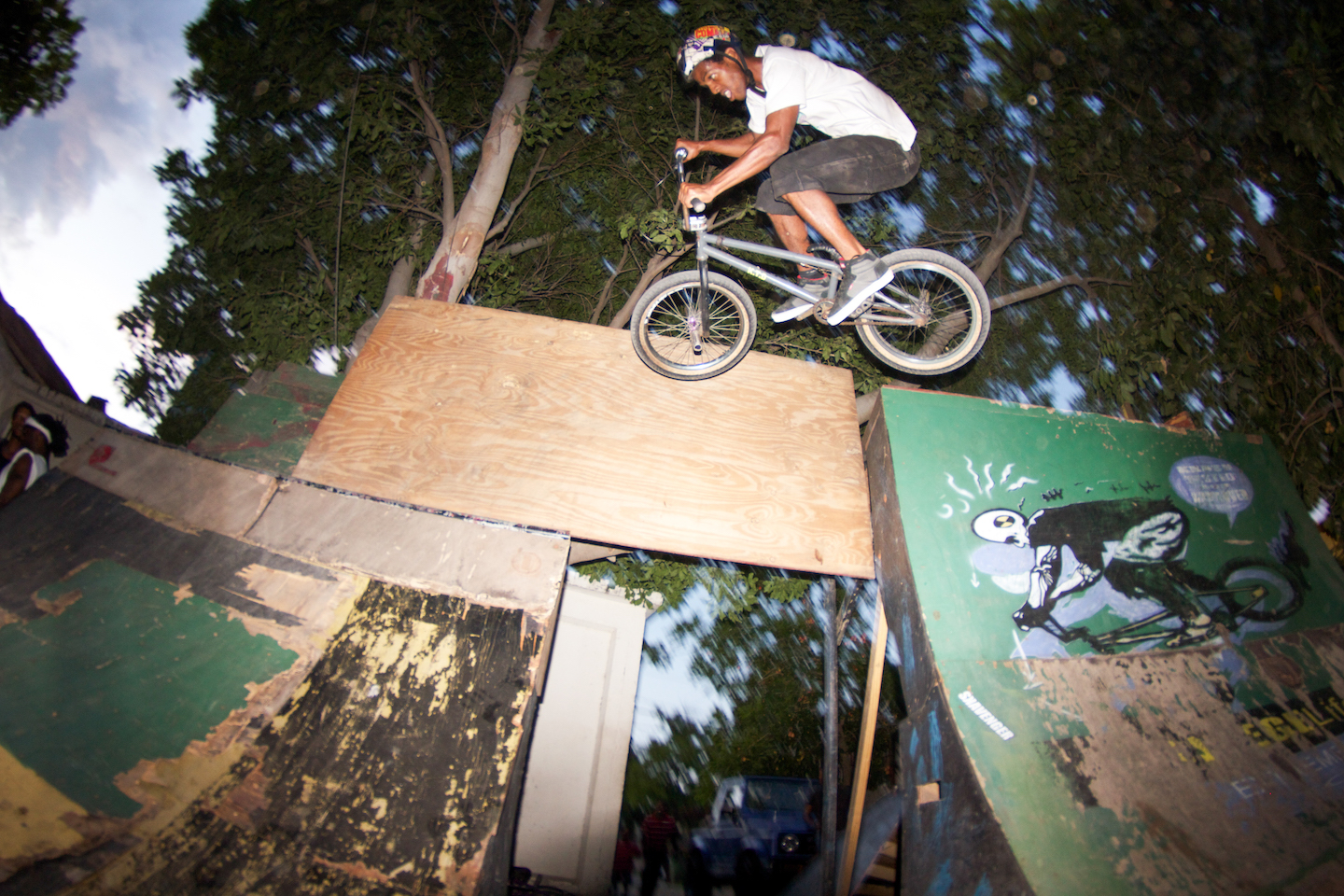 A man in a white t shirt and red helmet flies through the air on his BMX bike.