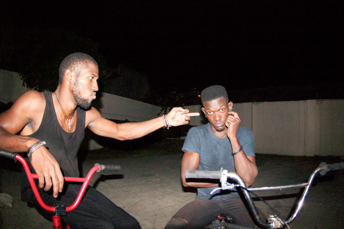 A man on a red BMX bike points his middle finger at another man on a black BMX bike.