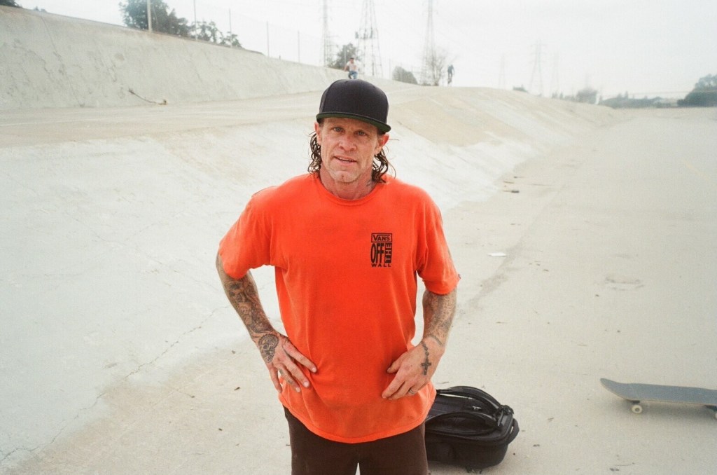 Pro skater Anthony Engelen stands in a half pipe wearing an orange t shirt.