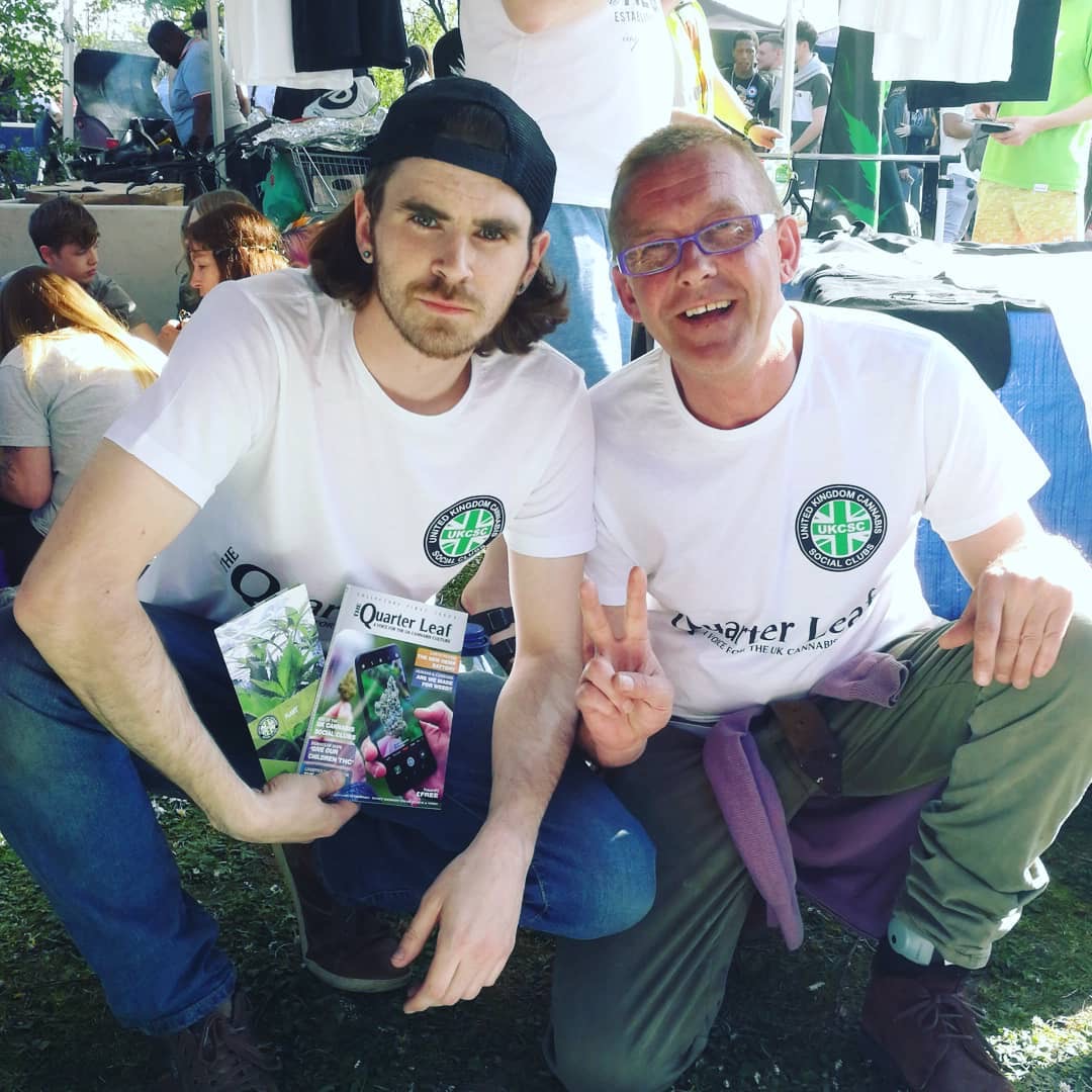 Two man kneel on grass showing flyers promoting cannabis growing