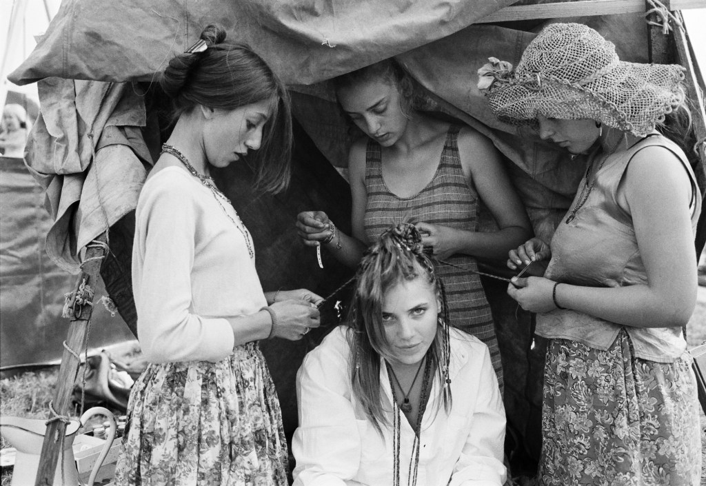 black and white photo of three girls braiding the hair of another girl