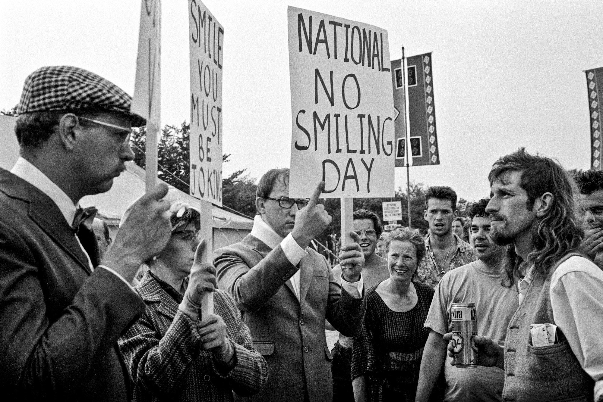 A crowd of people holding signs try not to smile at each other.