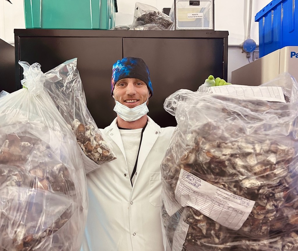 A scientist poses in a lab holding up two bags of mushrooms