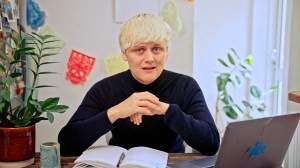 A man with blonde hair sits in front of a laptop and notepad