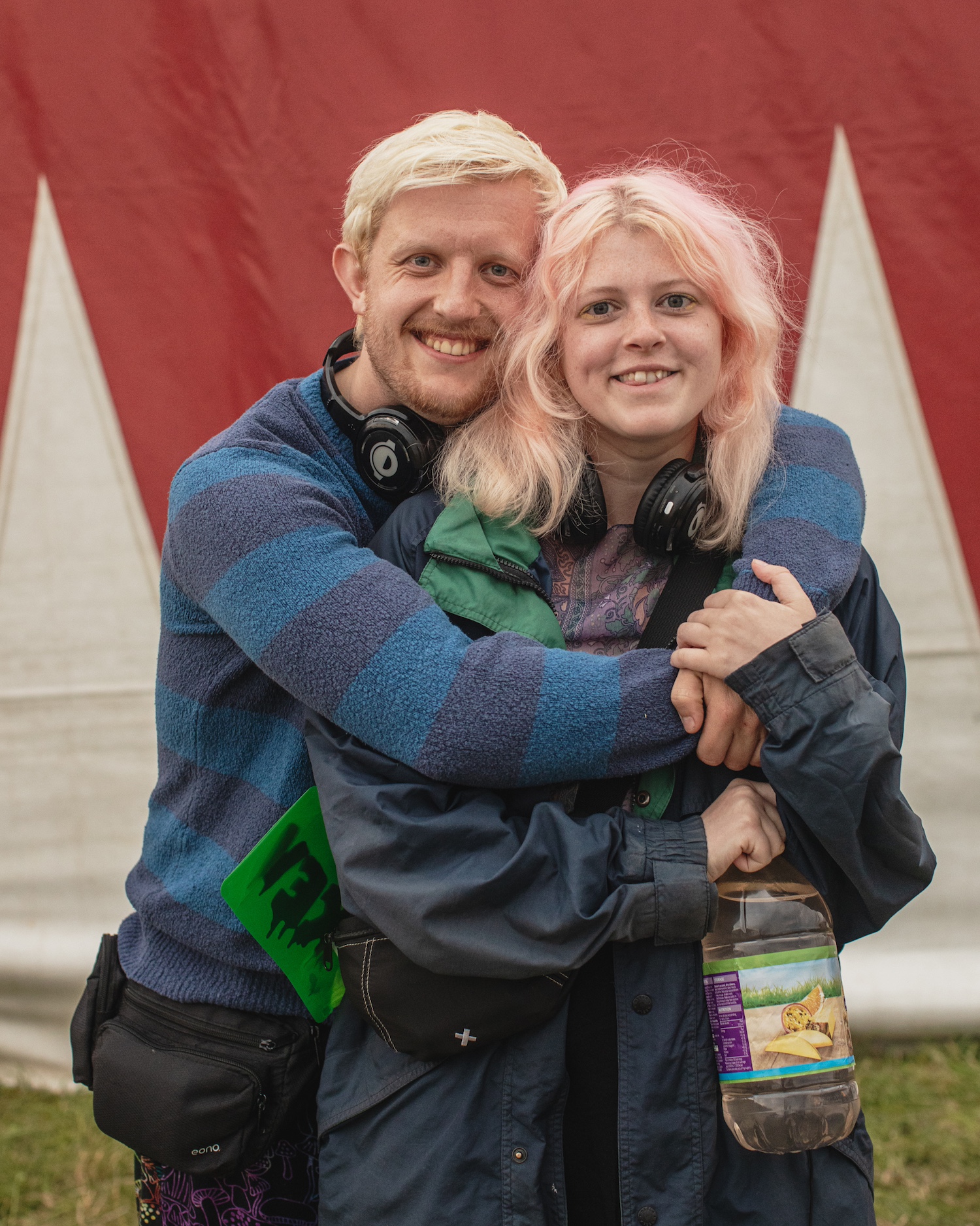 Two people with pink and white hair in front of a flag