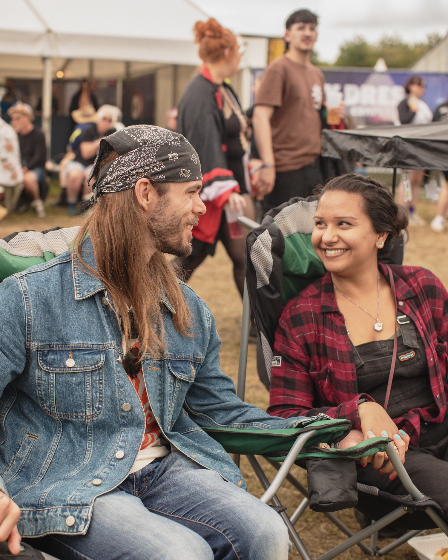 Two people in camping chairs at a festival looking into each other's eyes