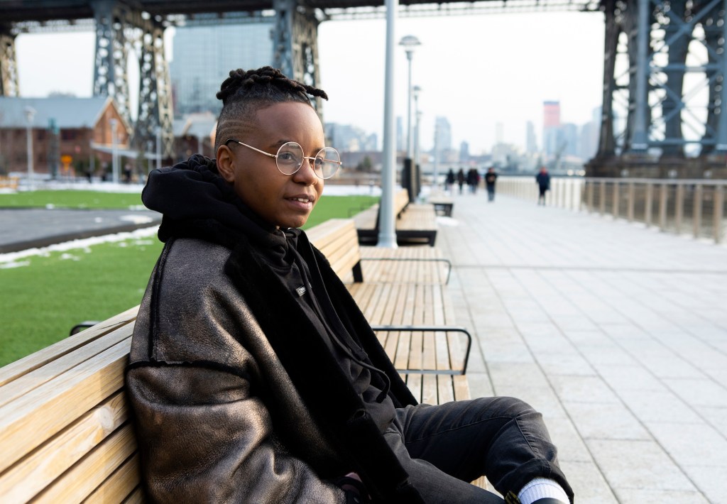 A transmasculine person sitting in a park and smiling_SMALL