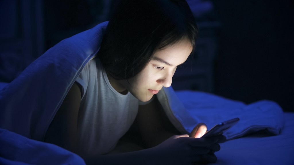 Portrait of teen girl lying in bed at night and using smart phone