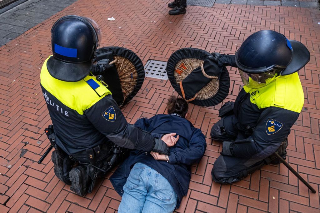 A man lays face down on the pavement while protesting in the red light district of Amsterdam, Netherlands, as two riot police with shields and helmets restrain him with handcuffs